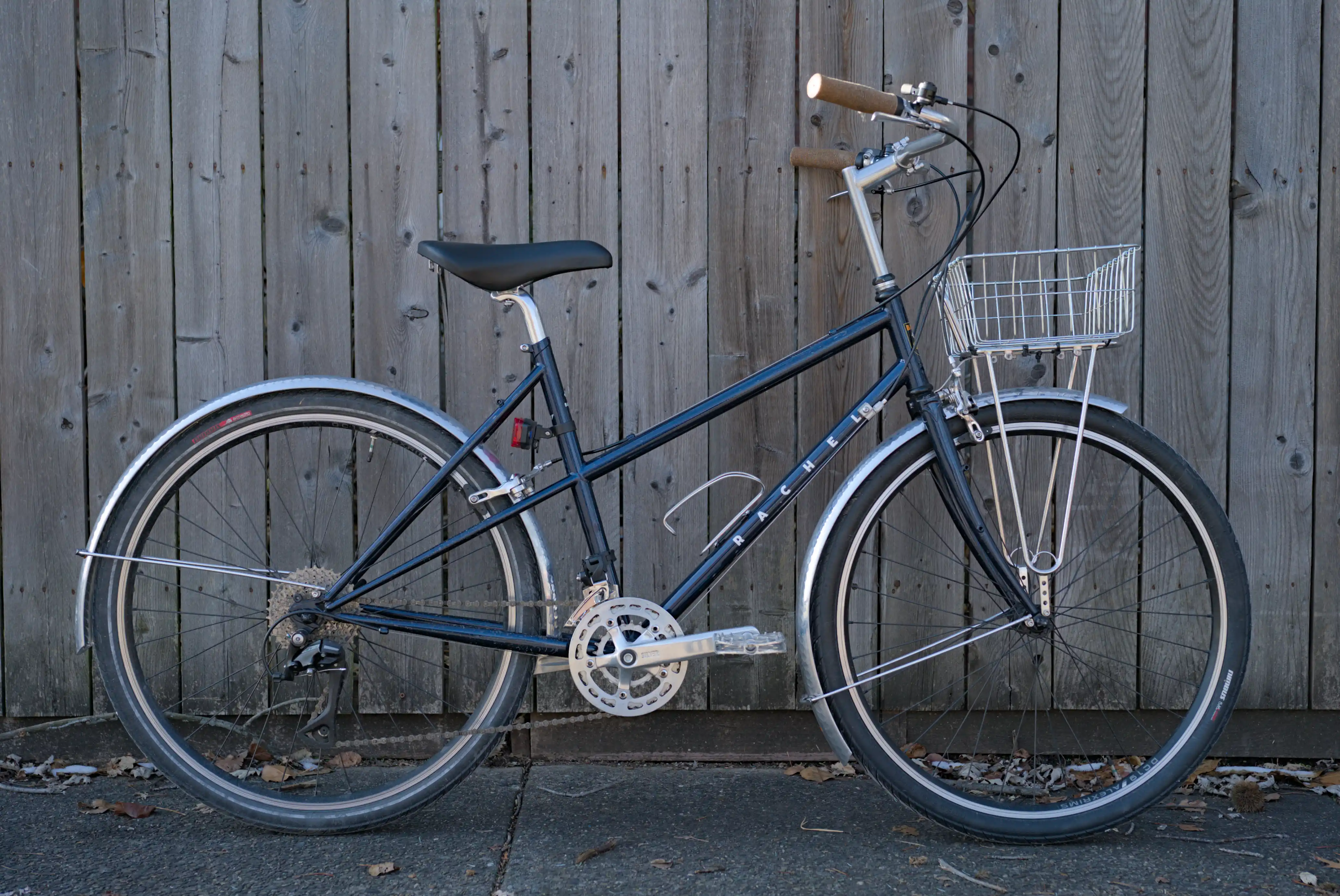 A dark blue bike leaning agaist a sun-bleached wooden fence.